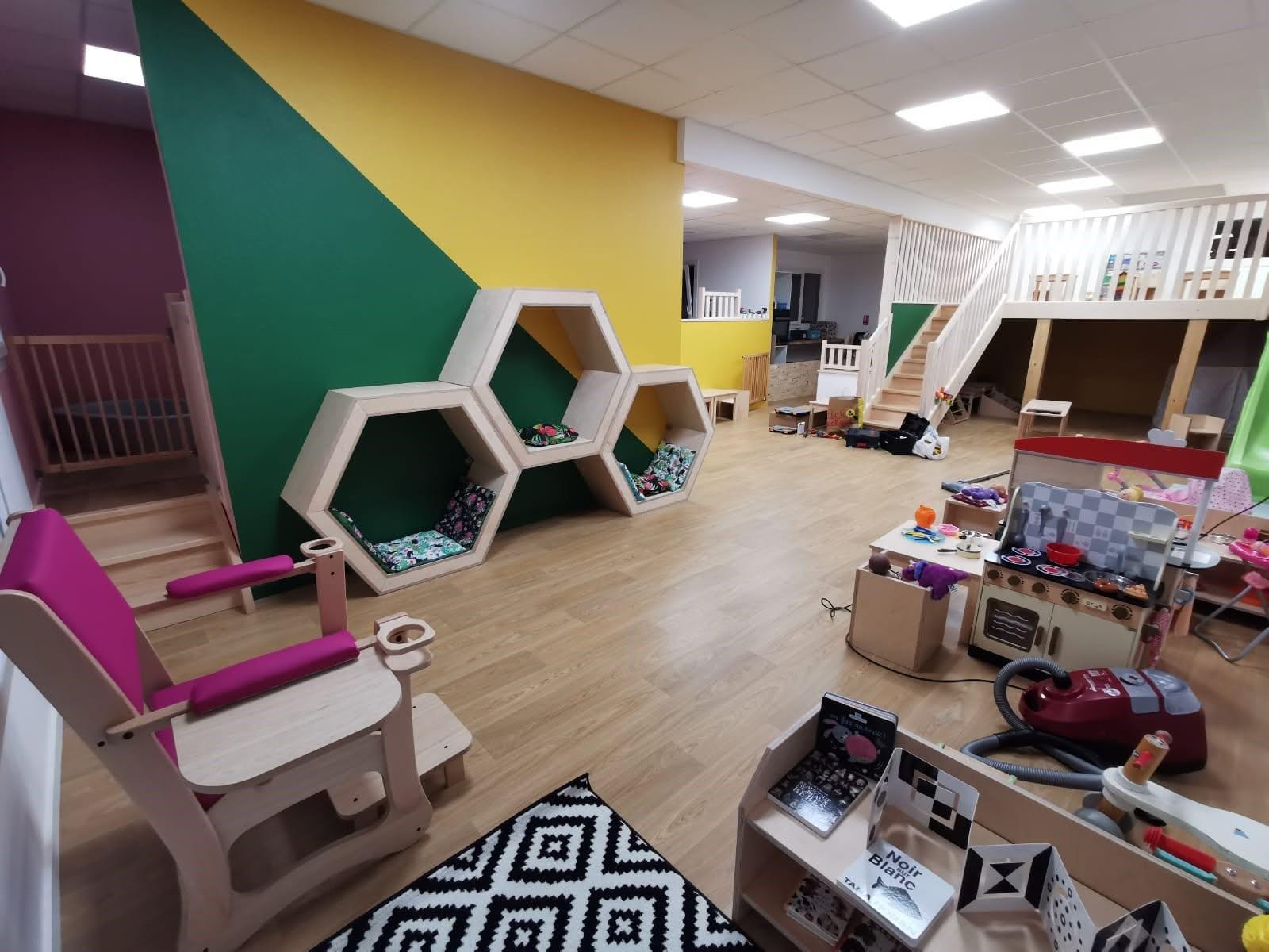 La salle de vie de la crèche : murs colorés, niches hexagonales en bois, mezzanine